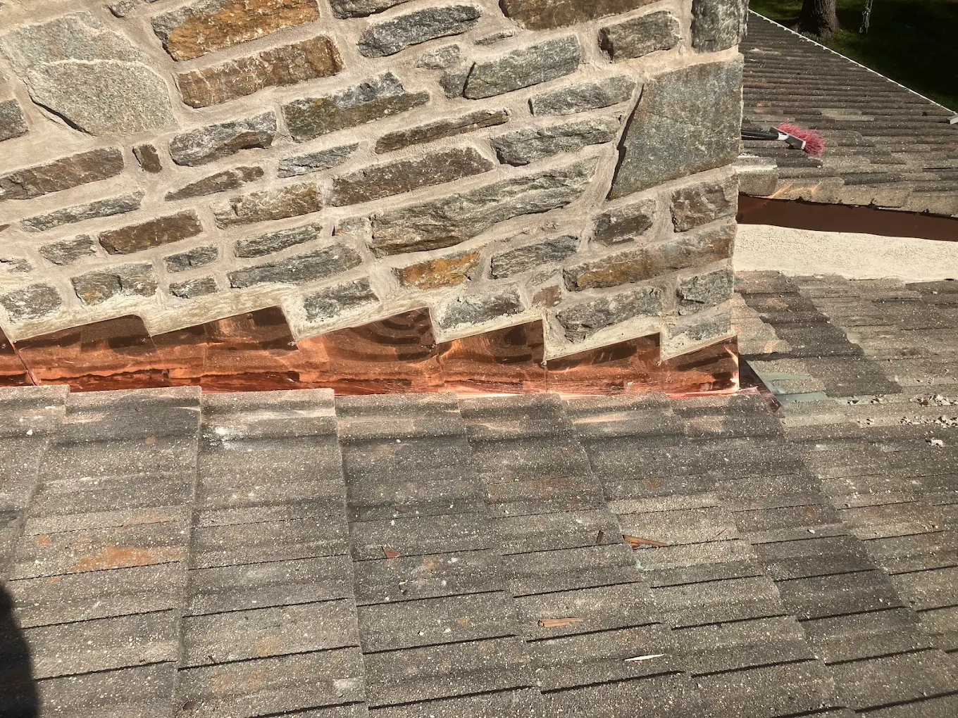 Custom copper flashing fitted around a stone chimney on a slate roof