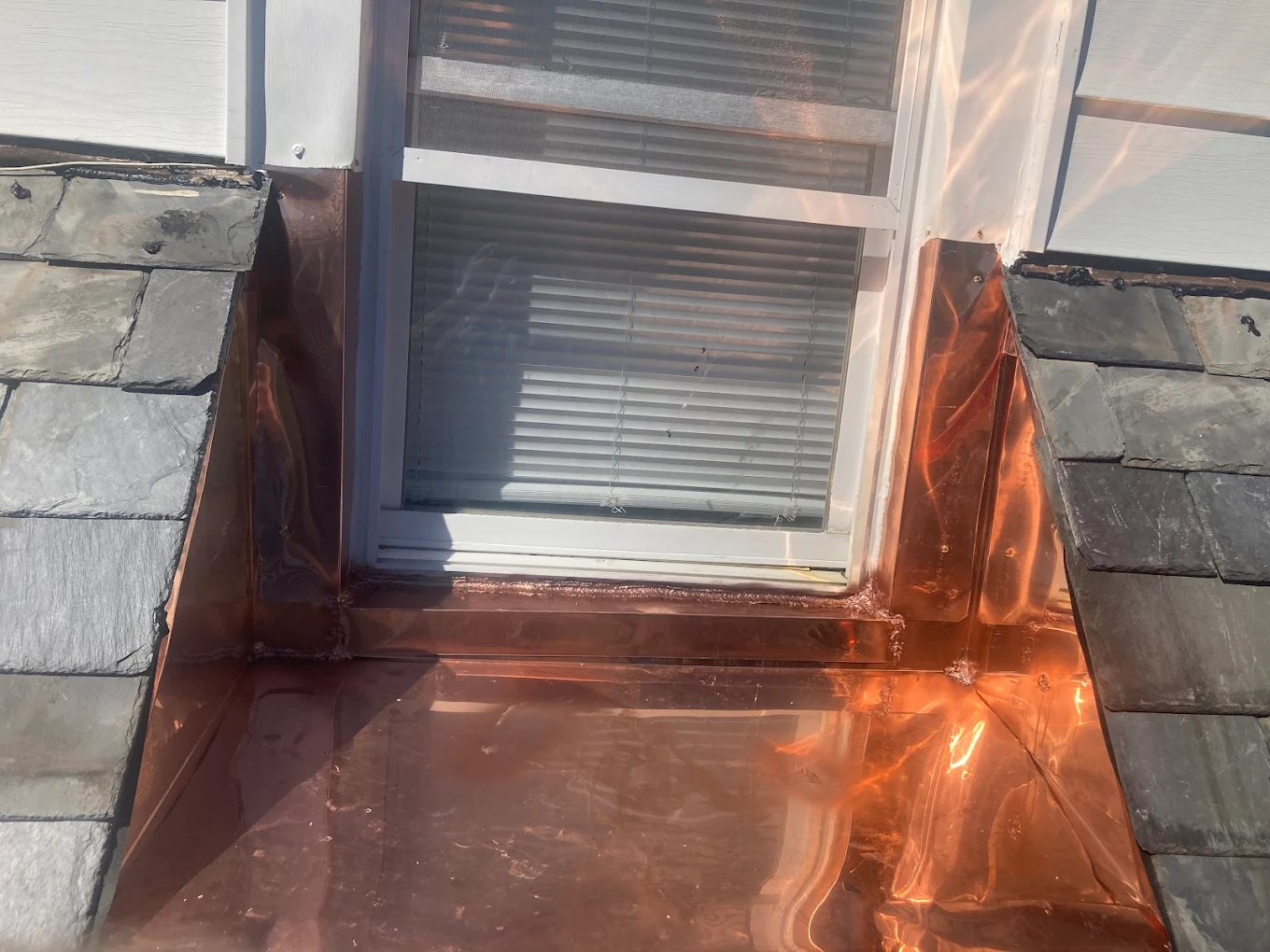 Hand-soldered copper flashing around a dormer window on a slate roof